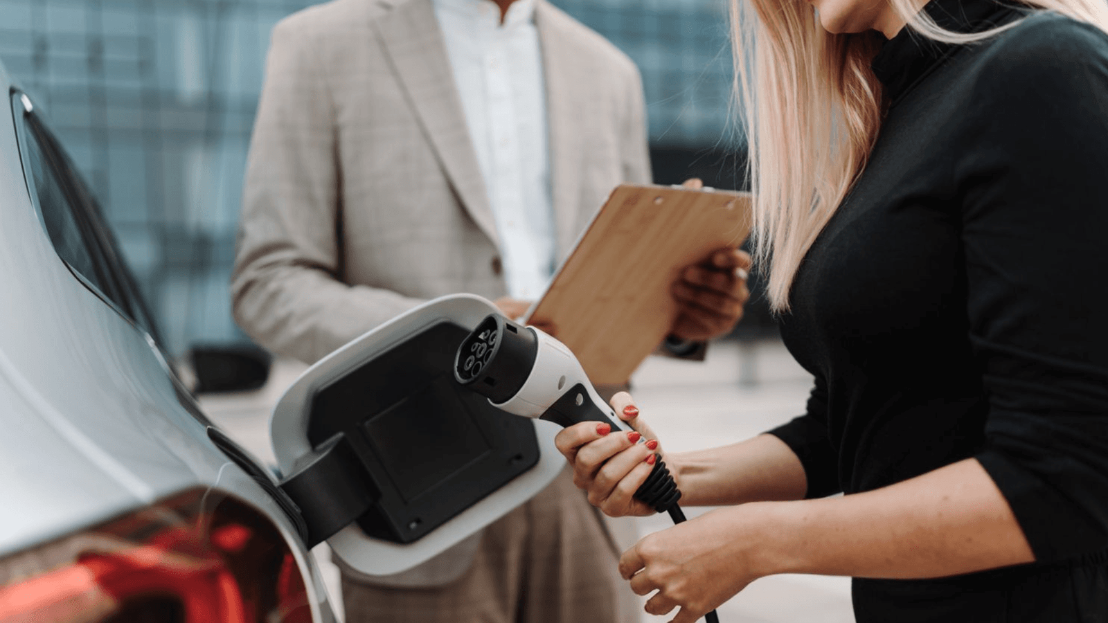 Electric Car Buyer Plugging in Charger During EV Purchase Inspection A woman connecting an electric vehicle charger while a salesperson with a clipboard reviews the EV purchase process at a dealership.